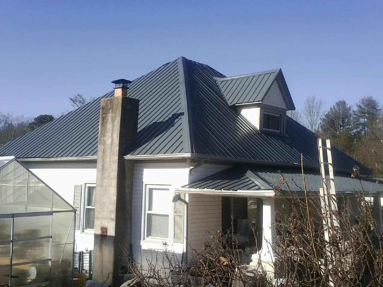 Dark blue standing seam metal roof on a white farmhouse with dormer — Slate & Tile Roof Repair by Roofing Brothers in Quail Valley