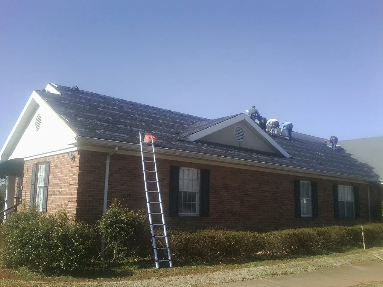 Crew tearing shingles off a brick ranch roof with a ladder set — Emergency Roof Repair work by our crew in Quail Valley