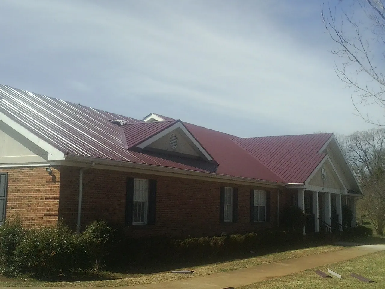 Red metal roof with gabled entries on a long brick building, from a Hail Damage Roof Repair job in Quail Valley