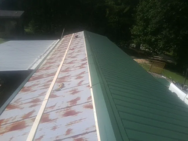 Old rusted panels beside newly installed green metal roofing — Wind Damage Roof Repair by Roofing Brothers in Quail Valley