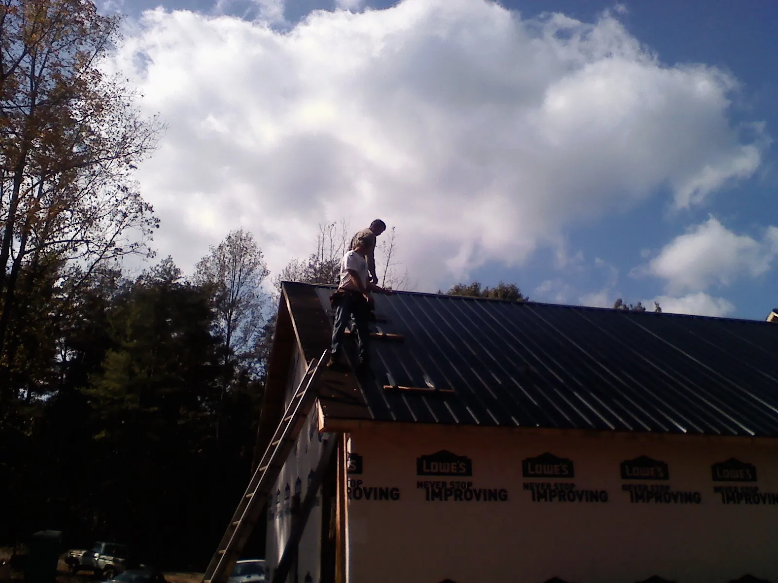 Roofer fastening dark metal panels high against a cloudy sky, from a Roof Inspection job in Quail Valley