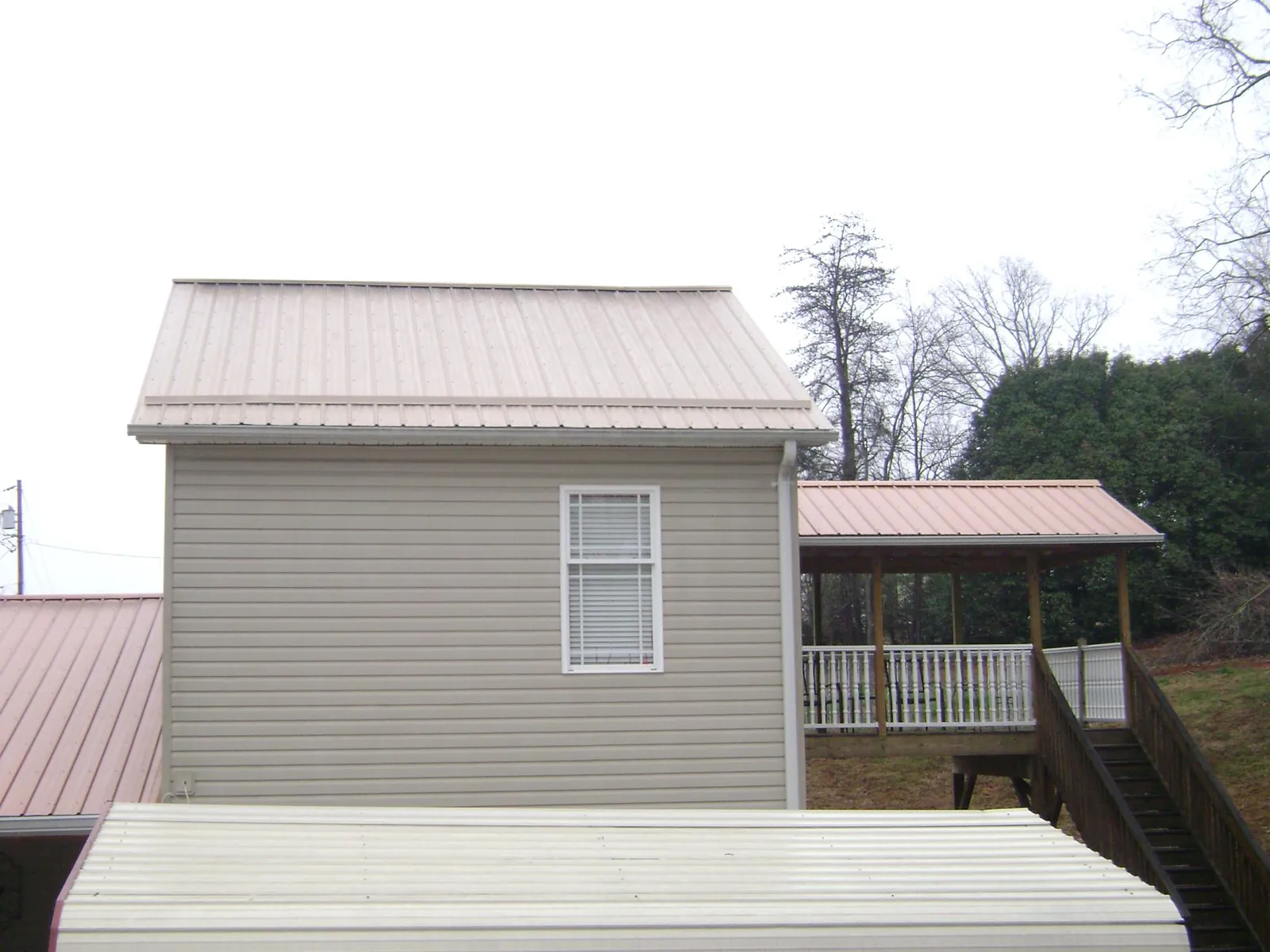 Tan metal roofs on a two story addition and attached porch, from a Roof Replacement job in Quail Valley
